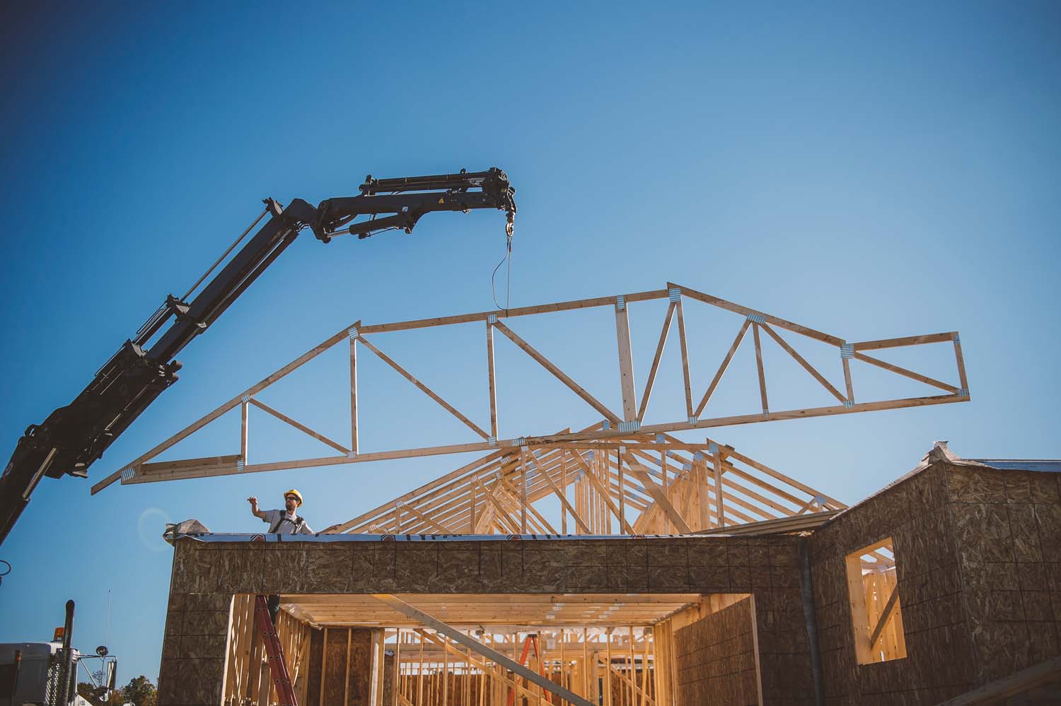 Builder directing crane positioning frame over building