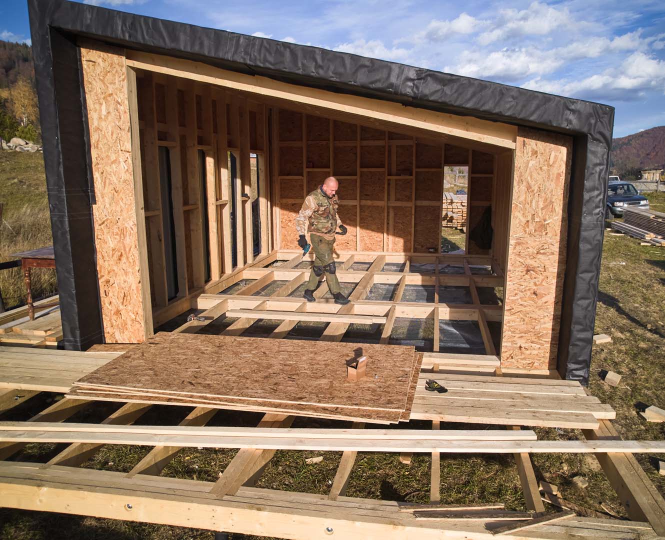 Male builder working with screwdriver inside of future wooden frame house.